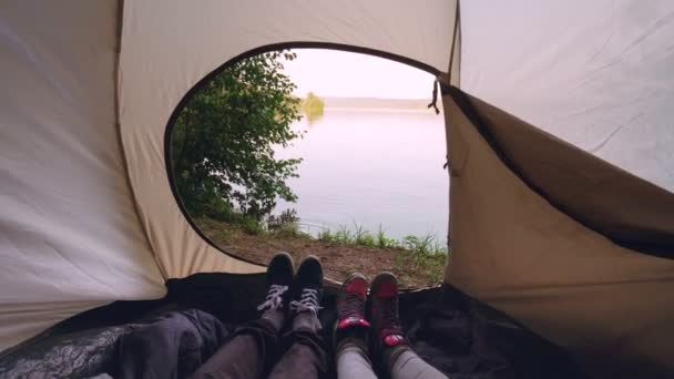 Туристы, лежащие в палатке, двигая ногами, делают танцевальные движения, наслаждаясь отдыхом, прекрасным видом на озеро или реку. Человек, природа и кемпинг . — стоковое видео