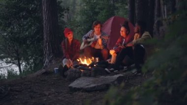 Kızlar ve çocuklar arkadaş şarkıları söyleyerek iken gitarist orman yangın yakındaki oturan ve doğa ve müzik zevk müzik aleti çalma. Çadır ve göl görülebilir.