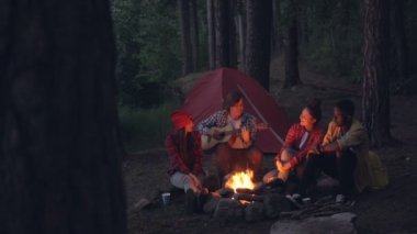 Arkadaşlar yürüyüşçü çok ırklı grup şarkı ve akşam kamp ateşi etrafında gülüyor gitar çalıyor. Yaz eğlence, Doğa ve eğlence kavramı.