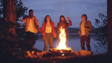 Heyecanlı genç erkekler ve kadınlar hipsters eğleniyor ormanda açık parti parlak kamp ateşi etrafında dans ediyor. İnsan, Doğa ve dostluk kavramı.