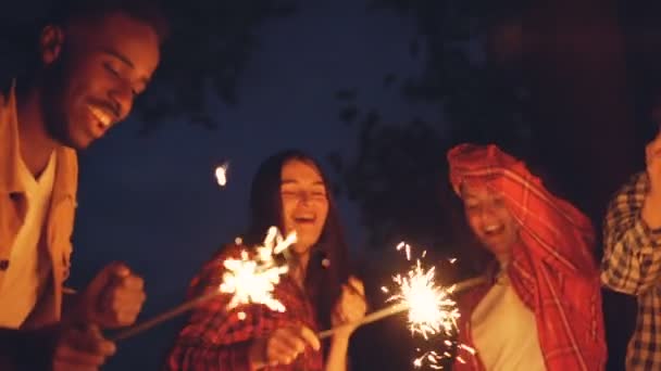 Медленное движение возбужденных молодых людей лучшие друзья танцуют с бенгальскими огнями на открытом воздухе и смеются весело. Празднование, дружба и молодежная концепция . — стоковое видео