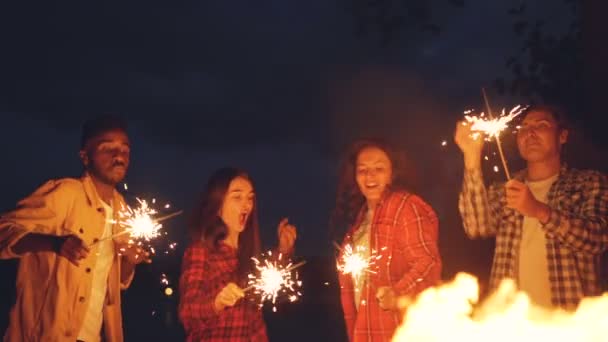 Mouvement lent des hommes et des femmes dansant et sautant à l'extérieur avec des étincelles brûlantes, s'amusant, célébrant des vacances et profitant d'une bonne compagnie. Les gens et le concept de divertissement . — Video