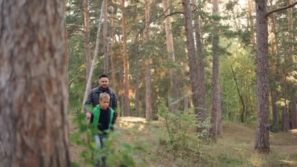 Zorgzame vader is wandelen met zijn mannelijke kindje in bos wandelen tussen bomen met rugzakken tijdens herfst weekend. Natuur, mensen en familie concept. — Stockvideo