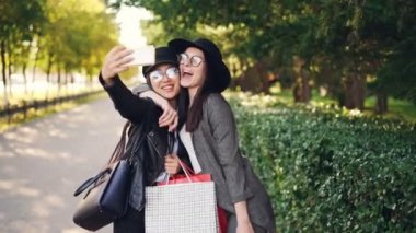 Heyecan arkadaşlar smartphone kullanarak ve alışveriş torbaları sonbahar güneşli satın almalarla holding selfie alıyor. Modern teknoloji ve gençlik yaşam tarzı kavramı.