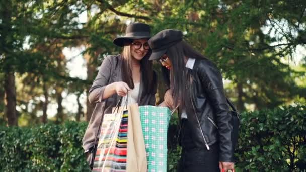 Δύο νεαρές γυναίκες shopaholics μιλάμε στο δρόμο κοιτάζοντας αγορές σε τσάντες και εκφράζει τον ενθουσιασμό. Ψώνια, άνθρωποι και ευτυχία έννοια. — Αρχείο Βίντεο