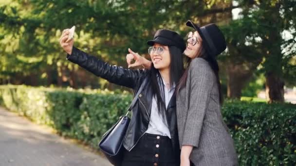 Las jóvenes adictas a las compras se están tomando selfies en la calle sosteniendo bolsas y haciendo caras graciosas. Las mujeres están usando prendas elegantes y gafas . — Vídeos de Stock