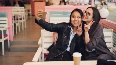 Güzel Asyalı kız selfie kafede masada oturan sonra fotoğrafları izlerken onun beyaz arkadaşıyla alıyor. Etnik dostluk, modern teknoloji ve Fotoğrafçılık kavramı.