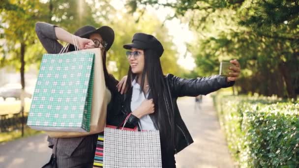 Giovani donne felici stanno facendo videochiamata online con smart phone parlando di shopping mostrando borse e ridendo in piedi in strada il giorno d'autunno . — Video Stock