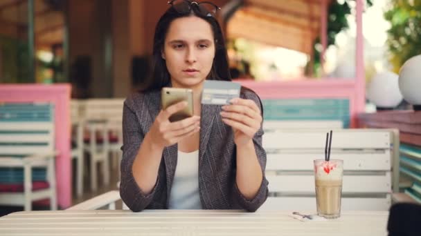Ganska ung kvinna håller bankkort och smartphone gör online betalning att röra skärmen då leende. Internet shopping och modern teknik koncept. — Stockvideo
