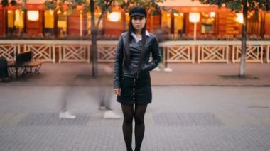 Güzel Asyalı kız açık havada hareket insanlar zaman trendy deri ceket cebine el ile ayakta kamera bakıyor, hızlandırılmış Yakınlaştır.