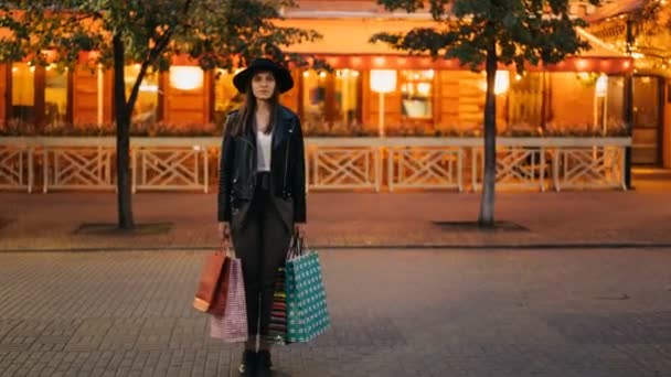 Zoom em time-lapse de menina bonita em roupas da moda em pé com sacos de compras na rua movimentada e olhando para a câmera quando multidões de pessoas estão passando . — Vídeo de Stock