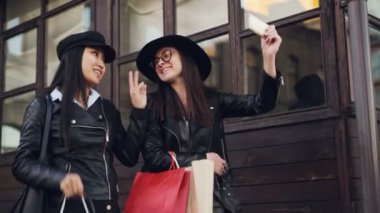 Güzel kızlar selfie smartphone ile alarak ve kağıt çanta sonbahar günü satın almalarla tutan arkadaşlar heyecanlı. Modern teknoloji ve gençlik kavramı.