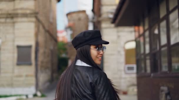 Медленно движущийся портрет привлекательной азиатки, идущей по улице с сумками, поворачивающейся, улыбающейся и смотрящей в камеру. Люди, концепция потребительского и городского образа жизни . — стоковое видео