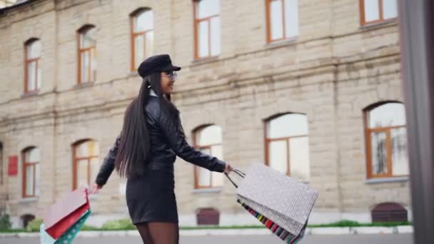 Retrato en cámara lenta de la mujer asiática feliz girando en la calle sosteniendo bolsas de regalo después del día de compras. Emociones positivas, estilo de vida juvenil y concepto de consumismo . — Vídeos de Stock