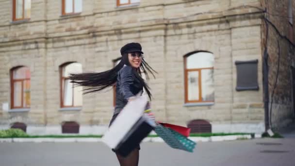 Медленно движущийся портрет веселой азиатской девушки с мешками для покупок, вращающимися на улице в современном городе, радующийся после посещения магазинов, веселящихся . — стоковое видео