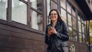 Çekici kız tek başına sokakta yürürken ve having fun smartphone tutan kulaklık üzerinden müzik ağır çekim. Gençlik ve modern teknoloji kavramı.