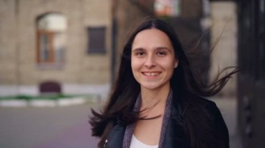 Ağır çekim portre kameraya bakarak ve ayakta açık havada arka planda caddenin ile gülümseyen güzel ve genç birbayan. Gençlik ve modern şehir kavramı.