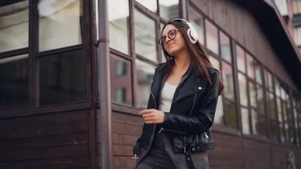 헤드폰으로 음악을 듣고 혼자 즐기는 인생을 걷는 도시에 거리에서 춤을 즐거운 여자 학생의 슬로우 모션. 청소년 문화와 기술 개념. — 비디오