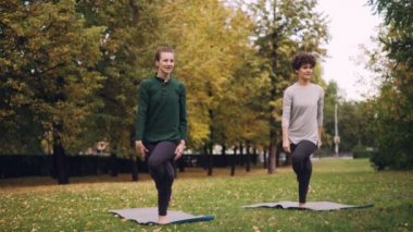 İnce kız yoga öğrenci öğretmen eğitmen Park ile rehberlik bireysel uygulamaları sırasında altında kartal poz öğreniyor. Güzel sonbahar doğa arka planda olduğunu.