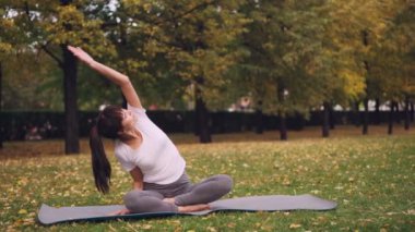Güzel kız yoga pratik mat lotus pozisyonu ve bükme yana doğru yükselterek kol parkta oturan konsantre olması. Sağlıklı yaşam tarzı ve eğlence kavramı.