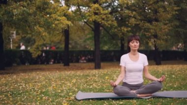 Çekici genç bayan yoga mat Park içinde mudra dizlerinin üzerine çöküp nefes üzerinde rahatlatıcı antrenmandan sonra elele lotus pozisyonda oturuyor. Meditasyon ve doğa kavramı.