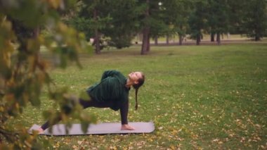 Yoga öğrenci yan açı konumu Parsvakonasana yoga mat Park varyasyonları pratik. Yeşil ve sarı ağaçlar, yapraklar ve çim görülebilir.