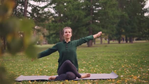 Cheerful lady is exercising in park sitting in Cow Face pose with arms behind her back during outdoor practice in city park. Nature, millennials and health concept. — Stock Video