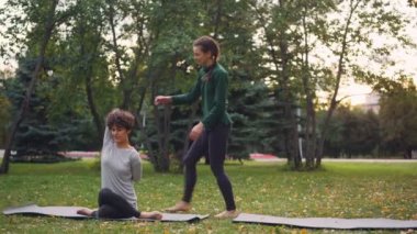 İnce kız yoga eğitmeni onu öğrenci bireysel uygulamada sonbahar park sırasında Gomukhasana yönetmek için yardımcı oluyor. Rehberlik, spor ve doğa kavramı.