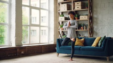 Genç ve güzel Bayan spor giyim pratik evde asanas Dengeleme tek ayak üzerinde tek başına duran yoga yapıyor denge üzerinde duruldu. Gençlik, aktif yaşam tarzı ve hobi kavramı.