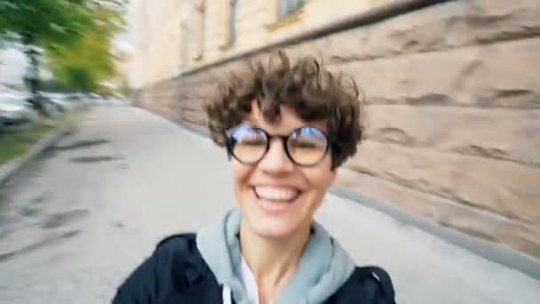 Punto di vista girato di spensierata giovane signora con i capelli corti e gli occhiali guardando la fotocamera e ridendo girando in strada divertendosi nella giornata autunnale . — Video Stock
