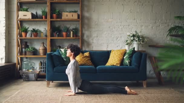 Zijaanzicht van slim meisje doet yoga thuis oefenen zon aanhef Surya eerste complexe op verdieping van mooi appartement. Gezonde levensstijl en jeugd concept. — Stockvideo
