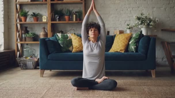 Zoom-in portret van aantrekkelijk meisje in de sport kleding zitten in de lotuspositie met handen in namaste dan zetten handen op knieën, ademen en rust. — Stockvideo