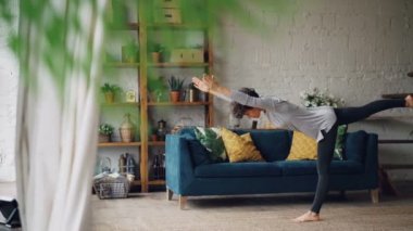 Aktif kişi bir bacak ayakta katta yalnız ev pratik denge egzersizleri yoga yapıyor. Güzel çatı stili mobilya ve tertibatları ile düz görünür.