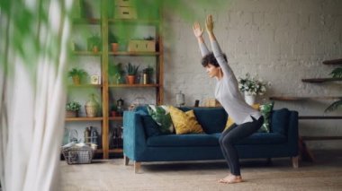 Genç ve güzel kadın evde eğitim sandalye yoga yaparken modern daire katta Utkatasana ayakta getirin. Kişisel uygulama, gençlik ve ev kavramı.