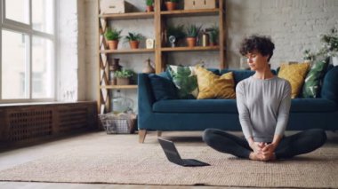 Güzel kız yoga Laptop hakkında online dersler izliyor ve kelebek egzersiz yaparak katta oturan evde yalnız pratik. Modern teknoloji ve gençlik kavramı.