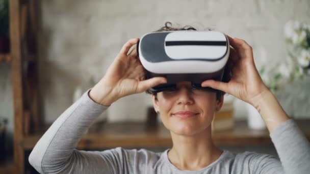 Close-up portrait of attractive curly-haired girl putting on augmented reality glasses and moving head and hands enjoying 3d video. People and fun concept. — Stock Video