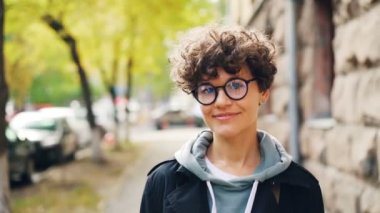 Ağır çekim gözlük ve rahat giyim gülümseyen ve kamera açık havada sokakta ayakta seyir çekici Bayan portresi. Gençlik, duygular ve şehir kavramı.