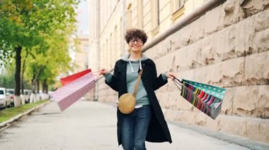 Ağır çekim alışveriş torbaları tutarak ve etrafında dönen mutlu kahkaha keyfi satınalma ve serbest zaman birlikte mutlu kıvırcık saçlı kız portresi. Shopaholism, gençlik ve şehir kavramı.