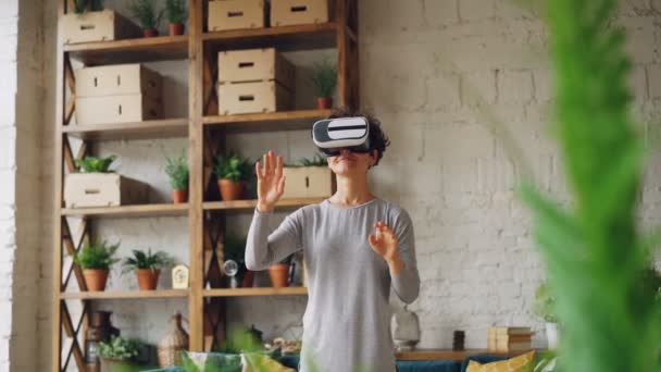 Amazed young lady is enjoying new experience in augmented reality glasses standing in flat and moving hands reaching in syberspace. Technology and fun concept. — Stock Video