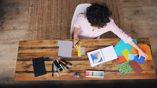 Pohled shora kudrnatý ženy dělat barevné papírové koláže, sedící u stolu řezání postavy s nůžkami. Design, kreativní lidi a interiéry koncepce. — Stock video