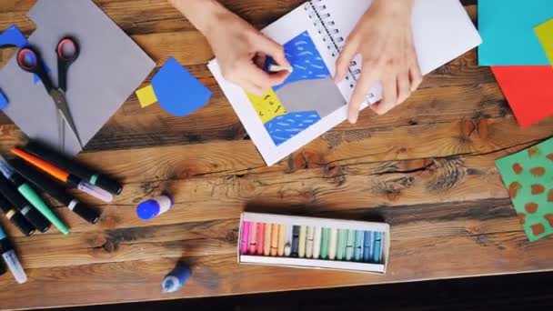 ホーム オフィスの机に座ってクレヨンでお絵かき用紙コラージュを作る創造的なブルネットのズーム アウト。アーティスト、専門家や職場のコンセプト. — ストック動画