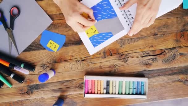 Genç kadının kapalı işyerinde masa başında oturan özgün kolaj yapma defter boya kalemi ile çizim zoom-out. Sanat, insanlar ve hayal gücü kavramı. — Stok video