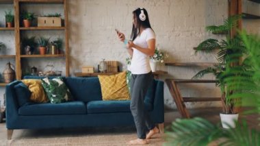 Çekici Asya Bayan smartphone kullanarak ve holding aygıt ve çay oturma odasında katta dans müzik kulaklık, dinlediği. İnsanlar ve eğlence kavramı.