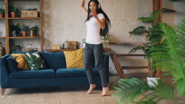 Radostné Asijská dívka tancuje na podlahu doma, spinning a jumping, poslechu hudby ve sluchátkách pomocí smartphone. Životní styl a radost koncepci pro mládež. — Stock video