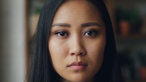 Detail slowmotion portrét atraktivní mladé asijské ženy perfektní pleť s vážnou tváří při pohledu na fotoaparát a pak s úsměvem, bílé zuby. — Stock video