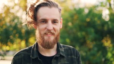 Ağır çekim portre sarı saçlar, sakal ve bıyık ayakta açık havada gülümseyen ve kameraya bakarak kaygısız biri. İnsanlar ve duygular kavramı.