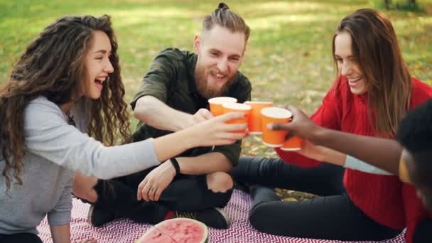 Slow motion van vrolijke meisjes en jongens vrienden rammelende bril tijdens picknick in het park, jonge mensen zijn praten en lachen proosten bedrijf dranken. — Stockvideo