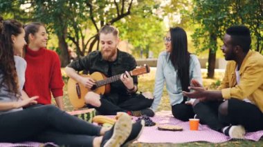 Arkadaşları eller alkışlar iken ağır çekim gitar çalmak ve sonbaharda park piknik üzerinde müzik keyfi mutlu öğrencilerin, gitarist oynuyor.