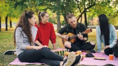 Arkadaşlar çok ırklı grup gitar ve şarkı alkışlayan eller serbest zaman ve sıcak sonbahar günü zevk oynarken parkta eğleniyor. İnsanlar ve müzik konsepti.