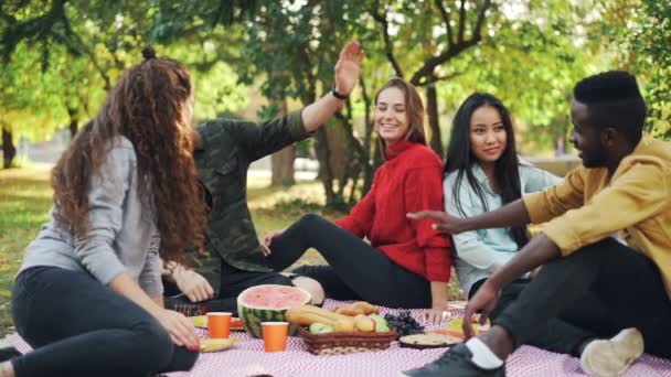 快乐的朋友的慢动作非洲裔美国人和白种人在城市公园野餐时做高五。友情、健康生活方式与连接理念. — 图库视频影像